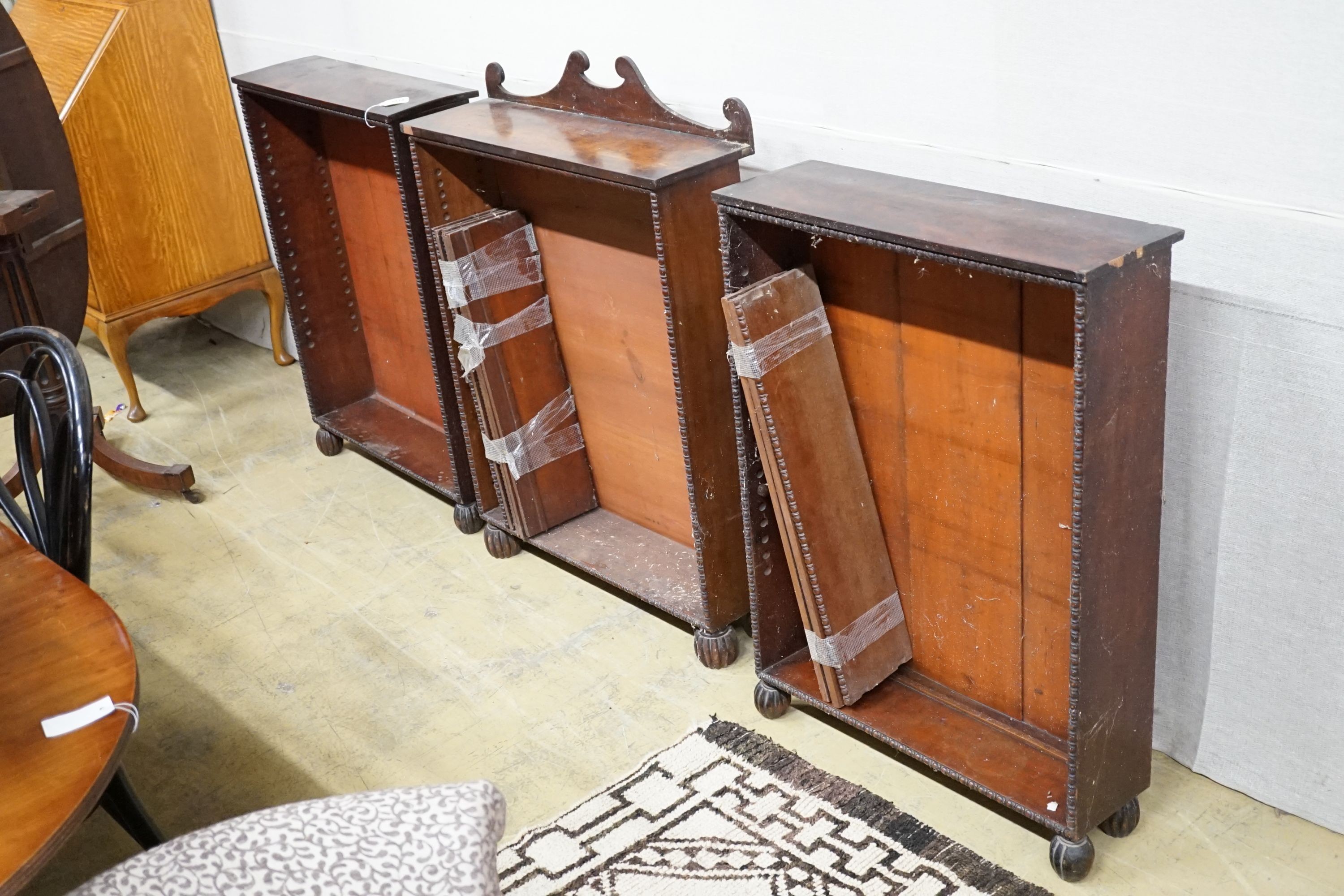 A set of three Regency mahogany open bookcases with beaded borders and fluted bun feet, one with crested back, centre bookcase width 72cm, height 103cm, wing bookcases width 66cm, height 92cm